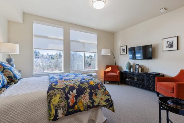 A bedroom with big windows, a dresser, two red chairs, and a television.