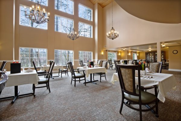 A large dining area with tables, chairs, chandeliers, and large windows.