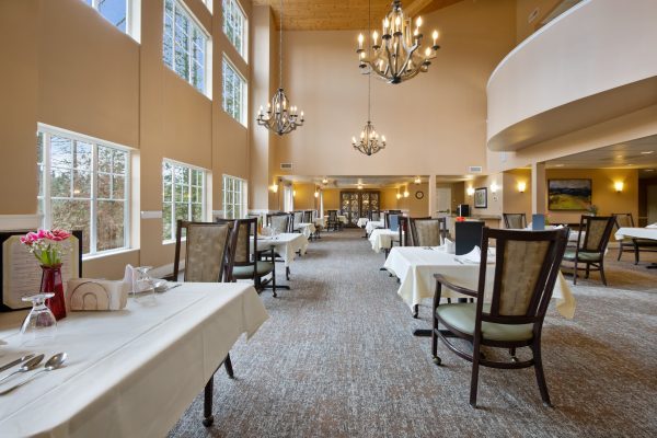 A large dining area with tables, chairs, chandeliers, and large windows.