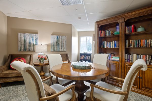 A seating area with a table and chairs and a large shelving unit with books in the background.