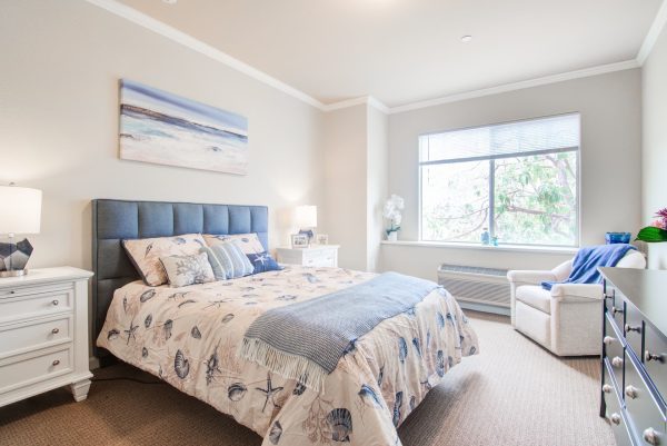 A large bed in a bedroom with a dresser, armchair, a window