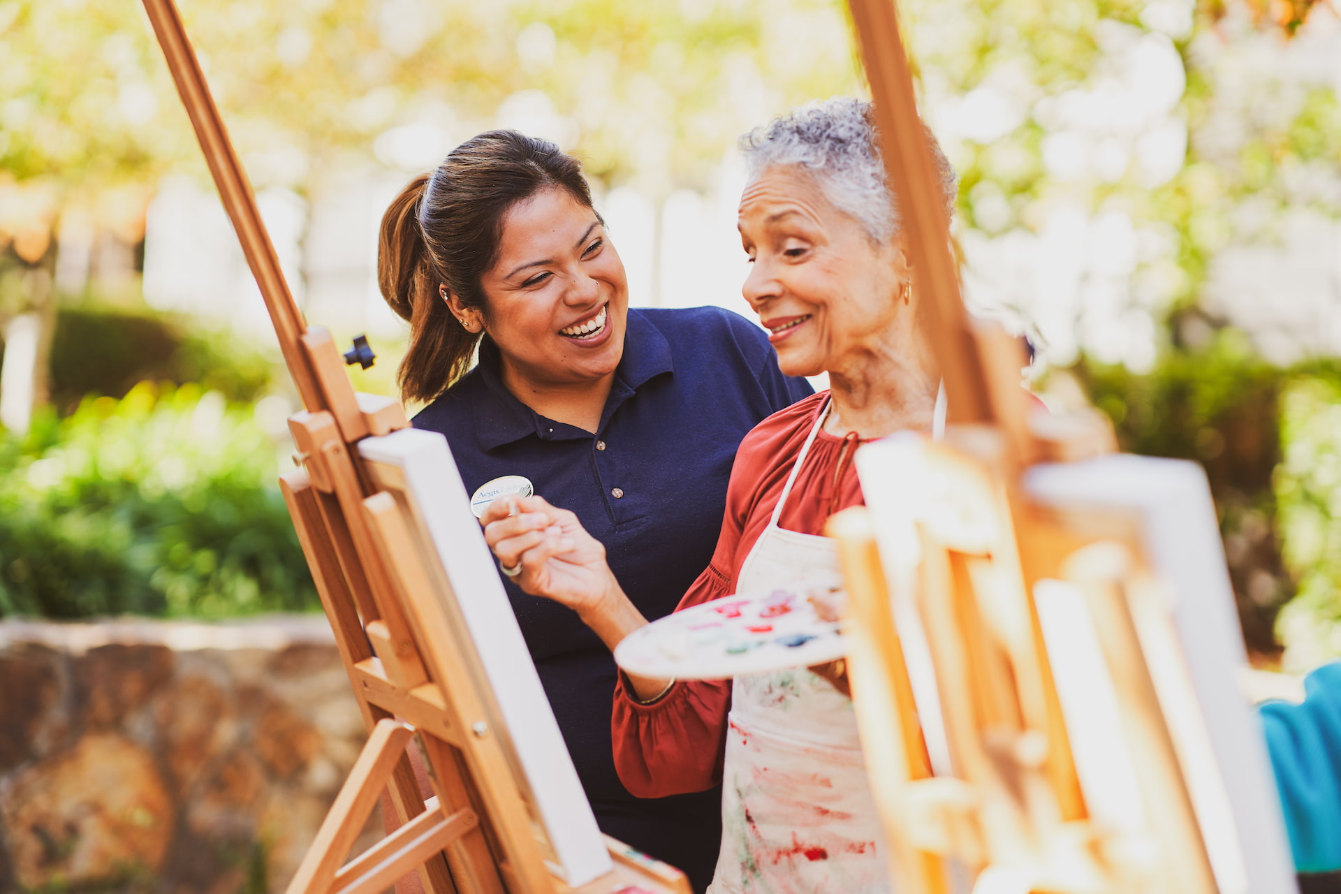 A resident painting a picture and standing beside an employee