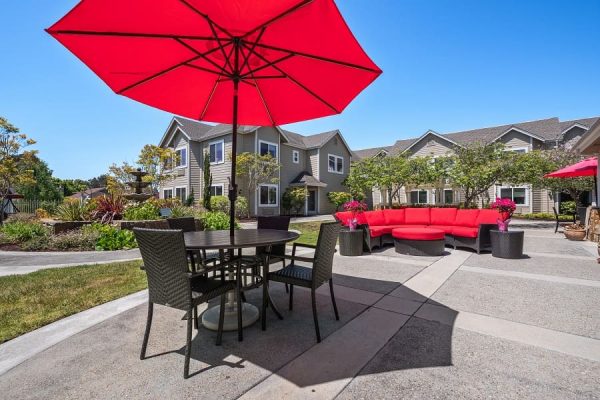 Two outdoor seating areas. One is a big red couch, and the other is a table, four chairs, and a red umbrella.