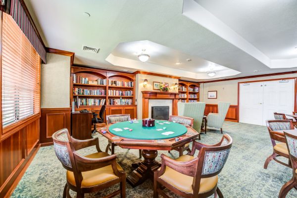 A game room with tables, chairs, and a built-in bookshelf with a fireplace in the background