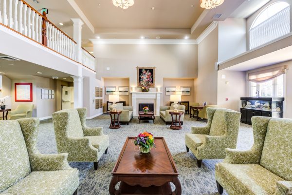 A large seating area with green armchairs, coffee tables, and a fireplace in the background