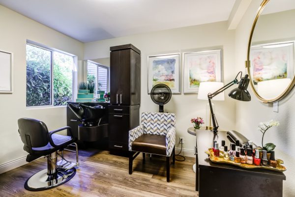 A salon with a salon chair, hair washing station, dryer chair, and manicure table