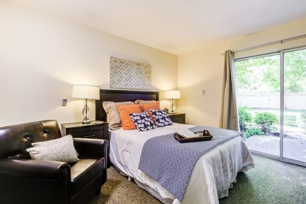 A bedroom with a bed, armchair, nightstands, and a sliding glass door