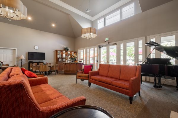 A large seating area with two orange couches, a grand piano, and lots of windows