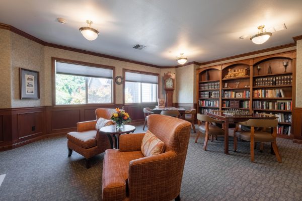 A library with two armchairs, tables and chairs, and a built-in bookshelf