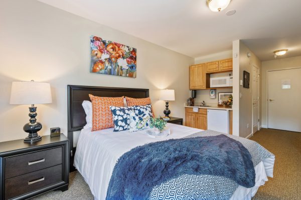 A large cozy bed with a small kitchenette in the background