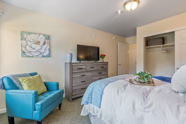 A bedroom with a bed, armchair, and television