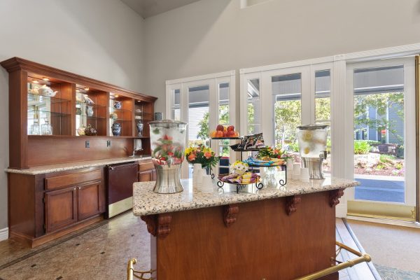 A small kitchen area with large windows and an island with water and fruit for the residents