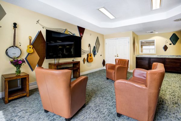 A music room with three armchairs, a television, and instruments hanging on the wall.