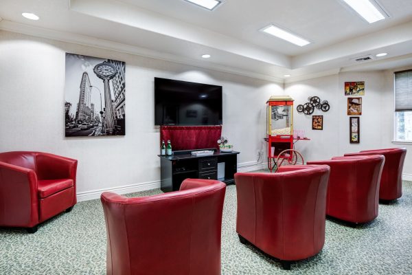 A movie room with four red armchairs, a television, and a popcorn machine.