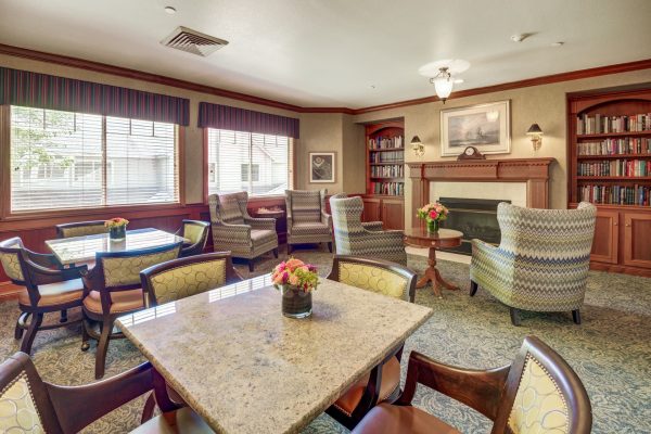 A seating area with tables, chairs, large windows, and a fireplace