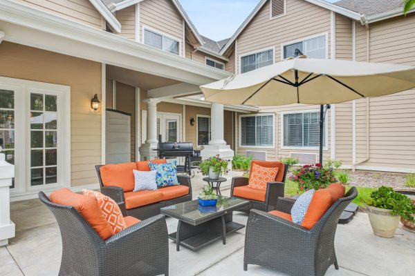 An outdoor patio seating area with orange cushions and a beige umbrella