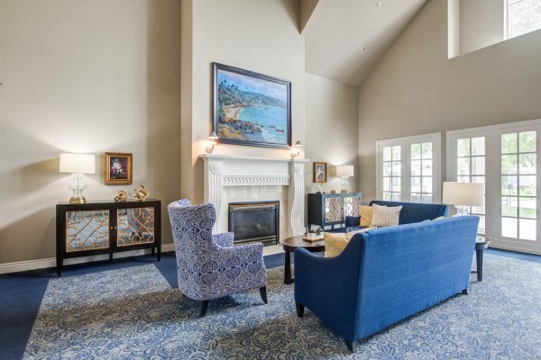 A large, brightly lit living room with blue couches, a blue and white chair, and a fireplace