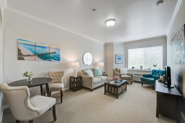 A living area with a large window, a couch, tables and chairs, and a television