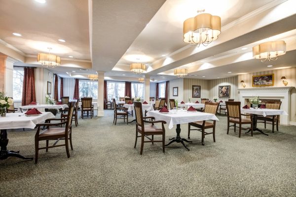 A formal dining area with tables, chairs, a fireplace, and windows in the back