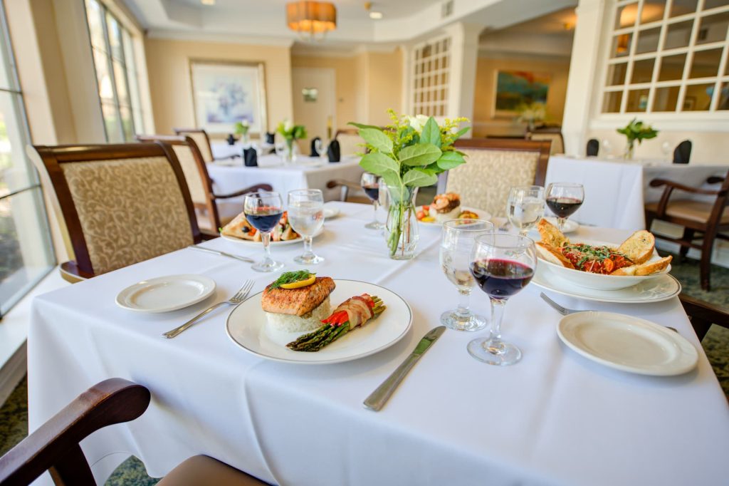 A close-up of a table set for four with plates of salmon and asparagus and four glasses of red wine