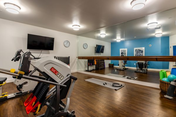 A gym with exercise machines, a mirror wall with barre, and a television