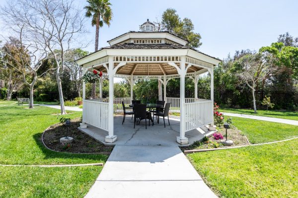 A white gazebo with a walking path and trees in the background