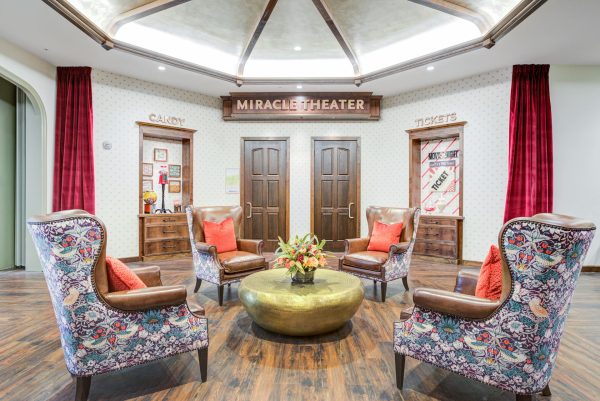 Four large armchairs around a gold coffee table with a sign that says “Miracle Theater” in the background