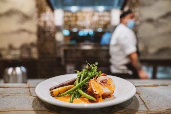 A artful plate of food with a chef in the background