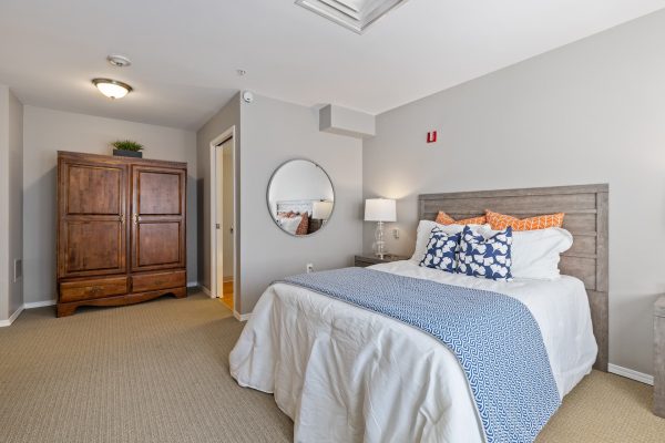 A serene bedroom with a bed, circular mirror, and armoire