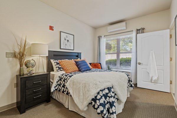 A bedroom with a cozy bed, large window, and nightstand