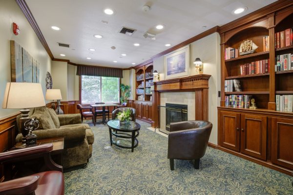 A library with a couch, chairs, tables, a fireplace, and a built-in bookshelf