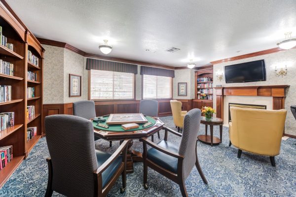 A room with a built-in bookshelf, table and chairs, and fireplace with a television above it