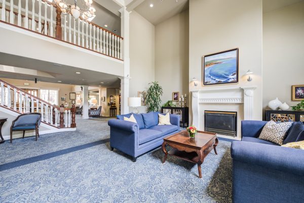 The lobby, featuring blue couches, a coffee table, and a fireplace, with a large staircase in the background