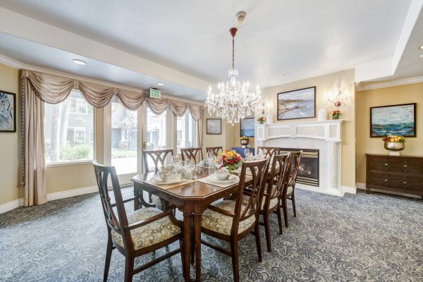 A large dining table with chairs, a fireplace in the background, and large windows to the side