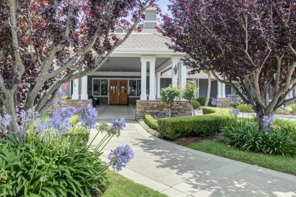 A close up of the main entrance, with a large pathway surrounded by flowers, shrubs, and trees