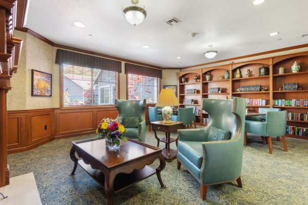 A reading room with large green armchairs, coffee tables, and a built-in bookshelf in the background.