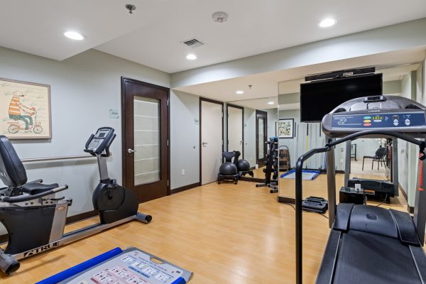 A workout room with a treadmill, stationary bike, mirror, and television