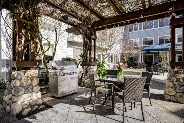 A covered outdoor dining area with tables, chairs, and a barbeque