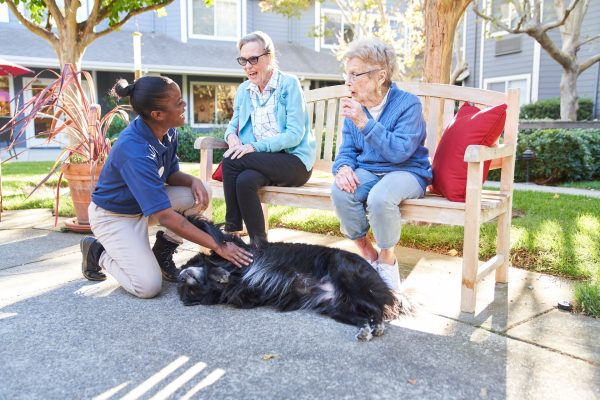 Two residents and an employee sitting outside petting a dog