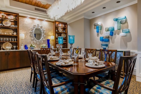 A dining table and chairs with a large horizontal chandelier hanging overtop and a mirror in the background