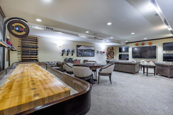 A games room with a shuffleboard table, tables and chairs, a couch, and a television