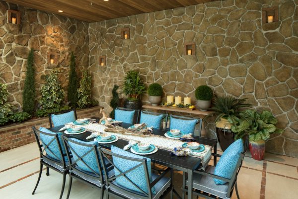 A large dining table with blue cushions on the chairs with a stone wall in the background