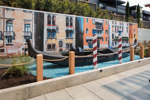 A black gondola sitting on a bed of blue rocks with a large photo of Venice in the background