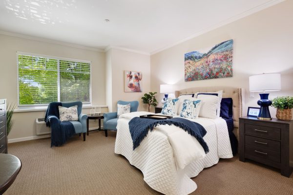 A bright bedroom with a cozy bed, two nightstands, and two blue armchairs