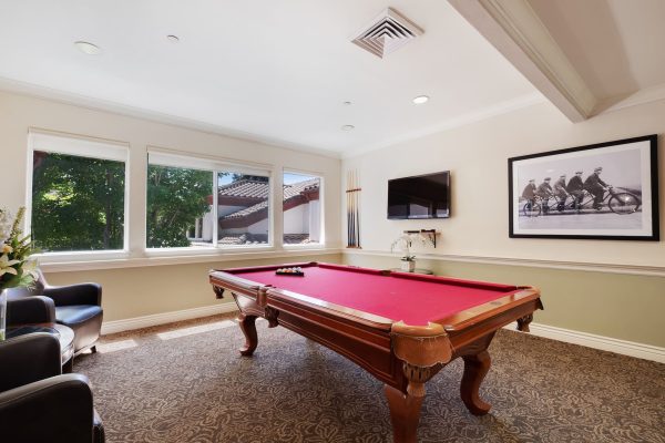 A billiard room with a pool table, two brown armchairs, and a television