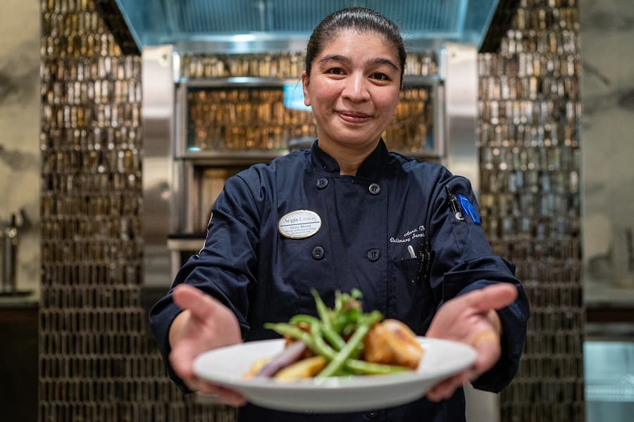 A chef holding out a plate of food and smiling at the camera