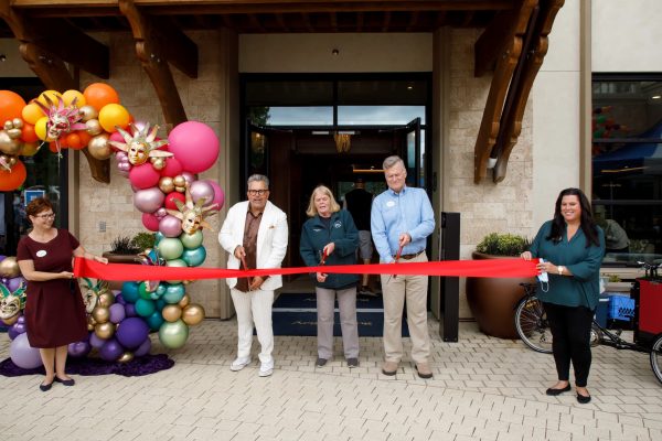 Three people cutting a red ribbon outside of Aegis Living