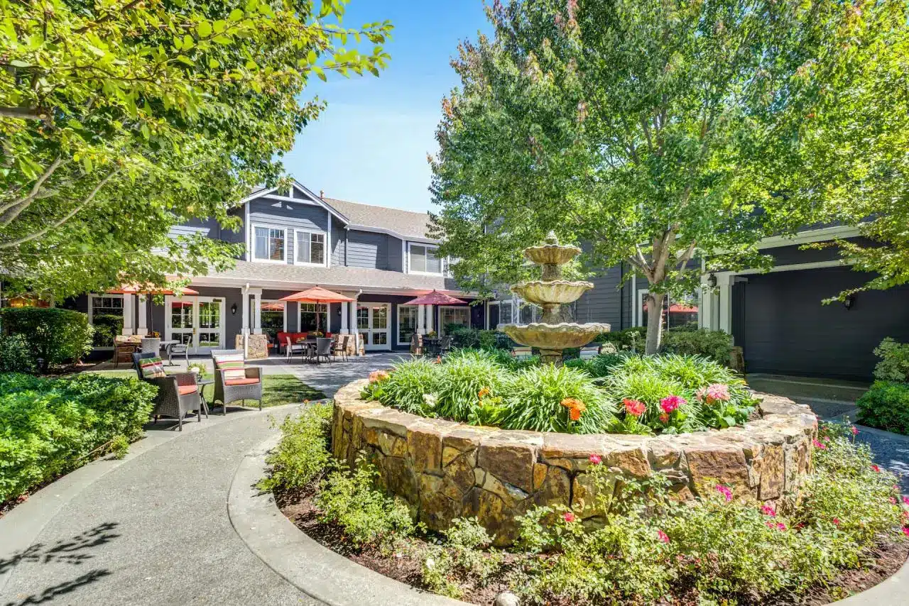 Beautiful flowers and greenery surround a fountain in the courtyard of an Aegis Living Facility
