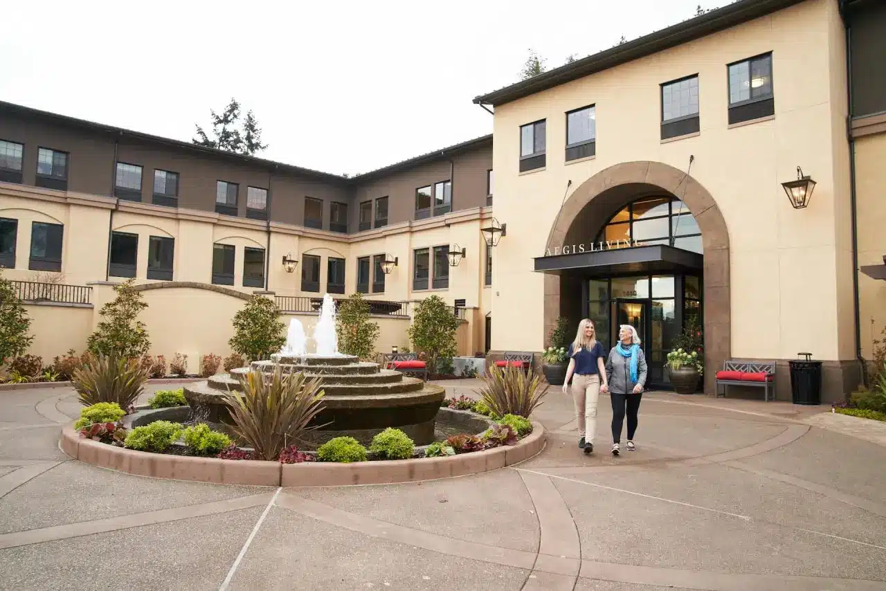 Senior and an Aegis caregiver walk outside of an Aegis Living facility