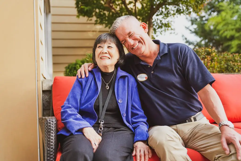 Two people smiling on a red couch outdoors.